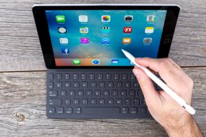 Laval, Сanada - April 3, 2016: Human hand using the new 9.7-inch iPad Pro space grey, isolated on a wood background with the Smart Keyboard and a Apple Pencil. Released March 31, 2016, this is Apple's latest iPad, and the first iPad Pro in the standard 9.7 inch size.